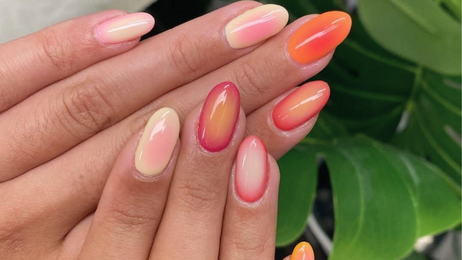 Short oval dip nails in glossy sunset ombre with pink, yellow, and orange aura blends on each nail.