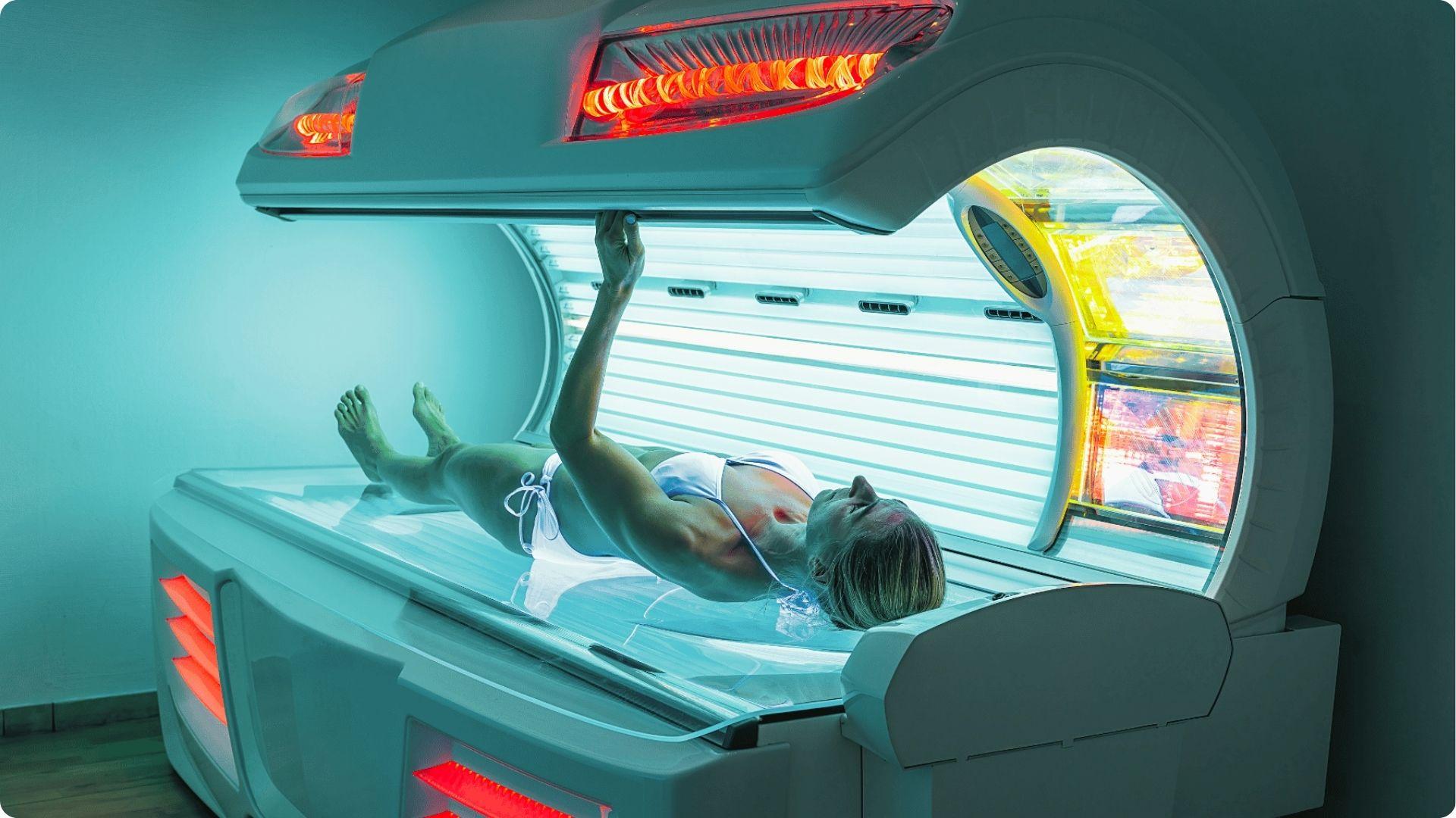 Woman in white swimwear using a tanning bed, reaching up to hold the canopy open.