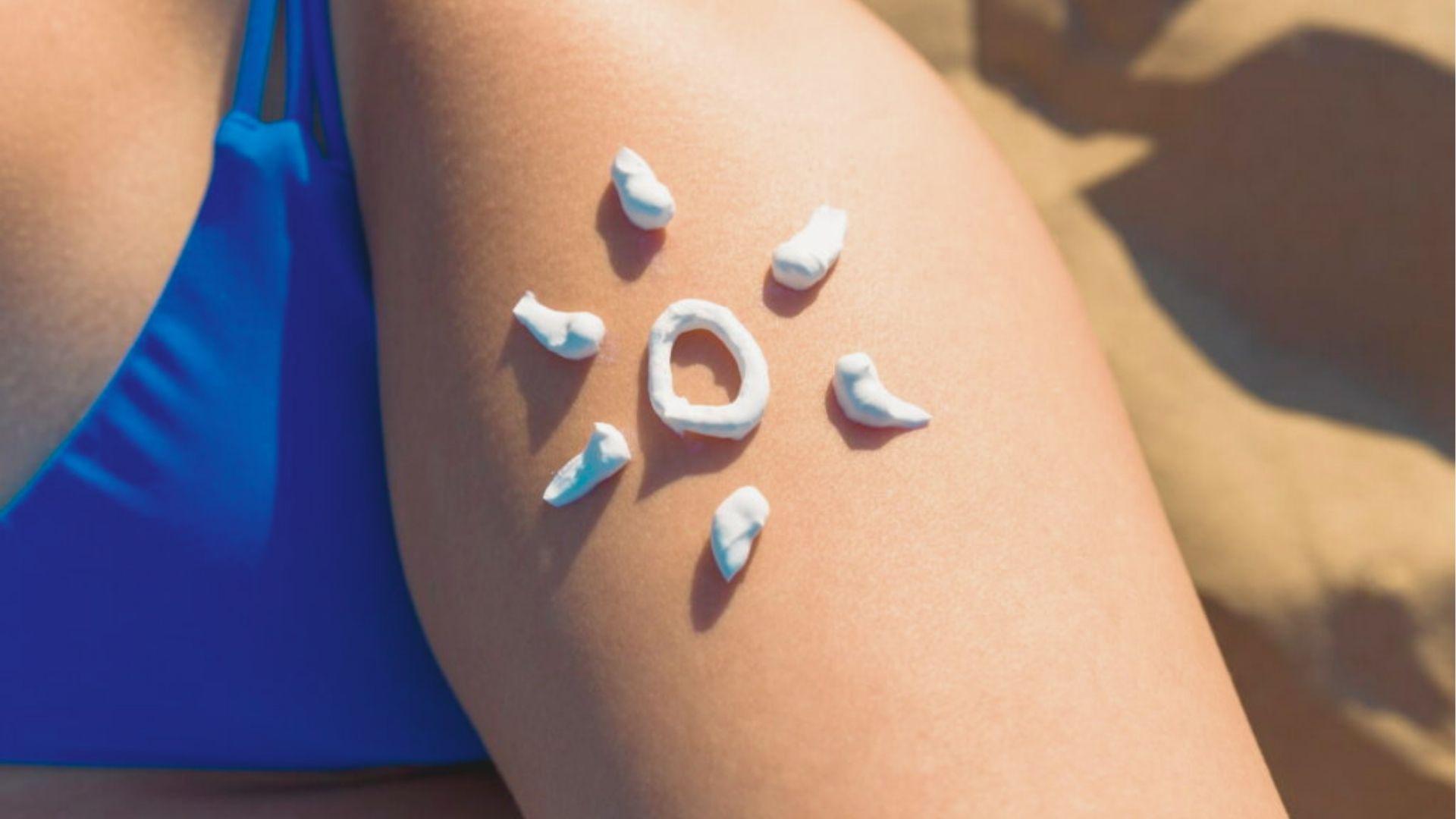 White sunscreen applied in a sun shape on a tanned leg in a blue swimsuit at the beach.