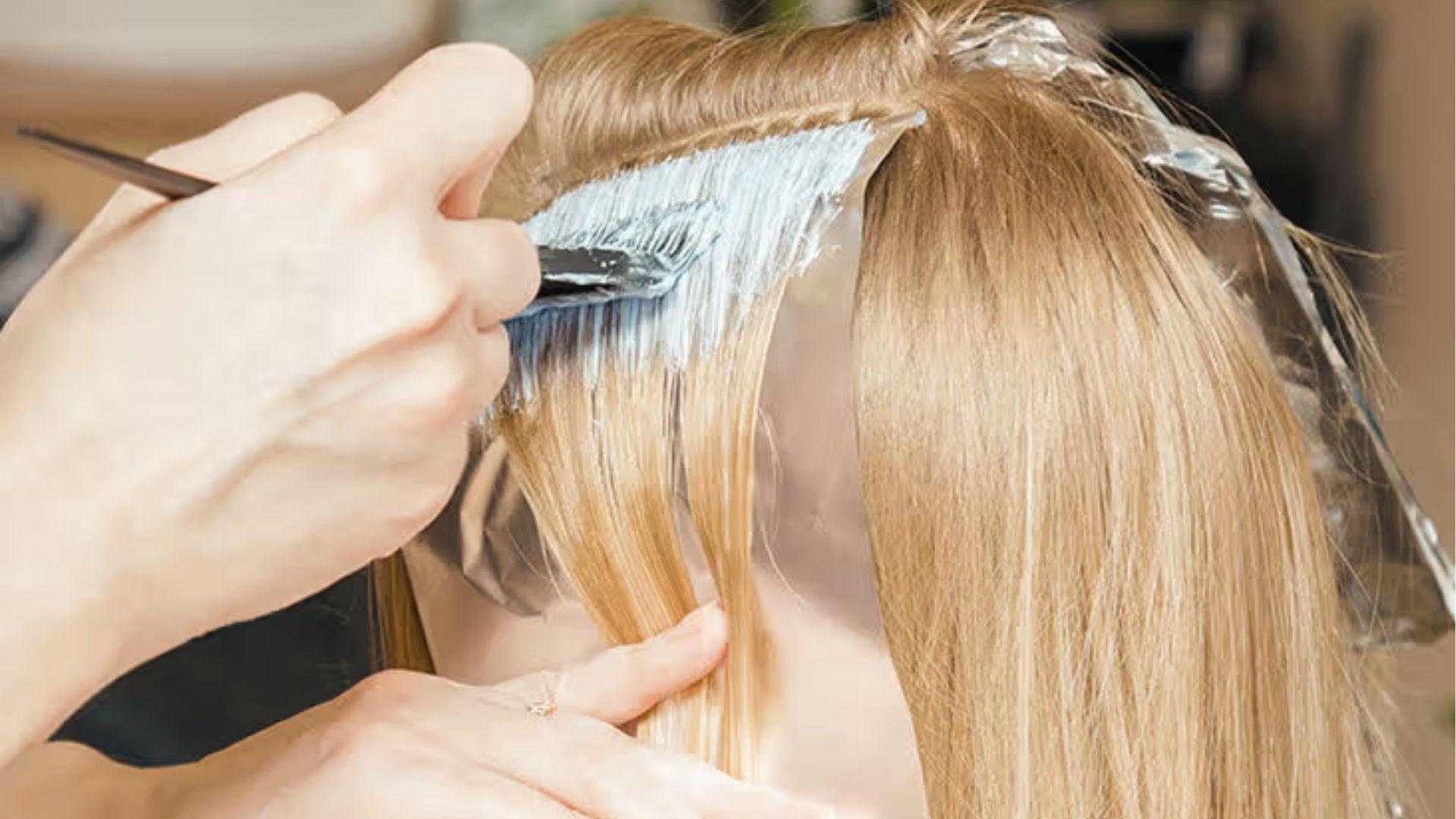 Stylist brushing bleach on sectioned hair over foil, tracking processing time to prevent damage.