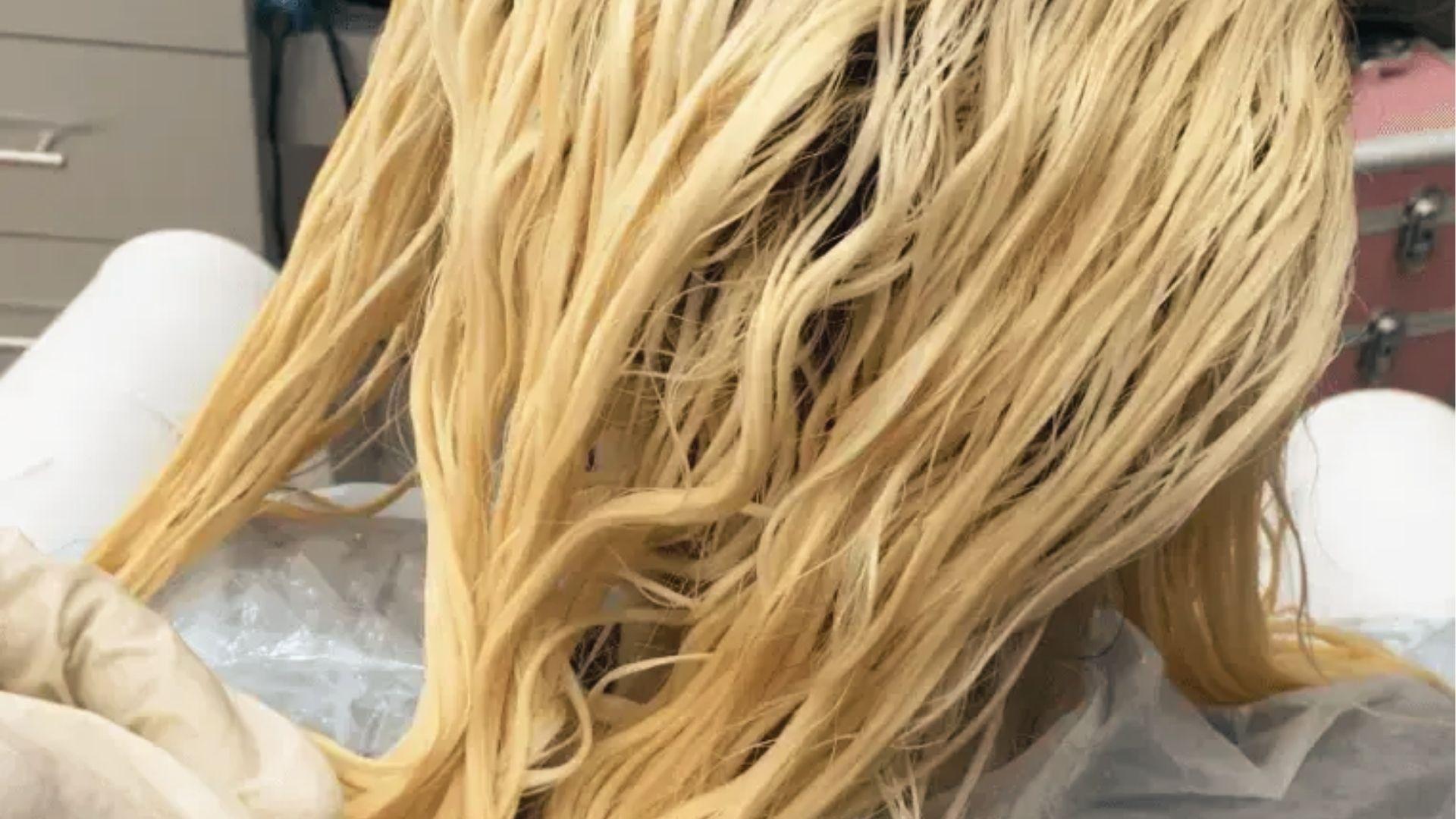 Woman rinsing bleached hair at salon sink while stylist checks if processing time is complete.