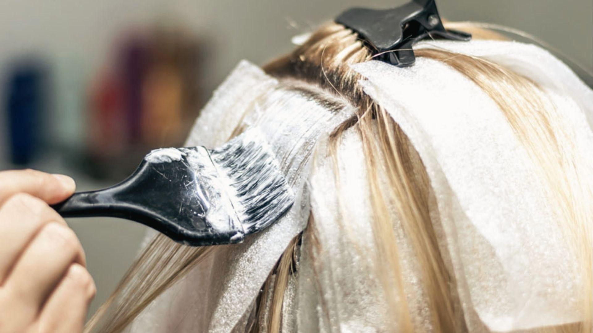 Stylist applying hair bleach with brush to sectioned blonde hair over foil for even lightening.