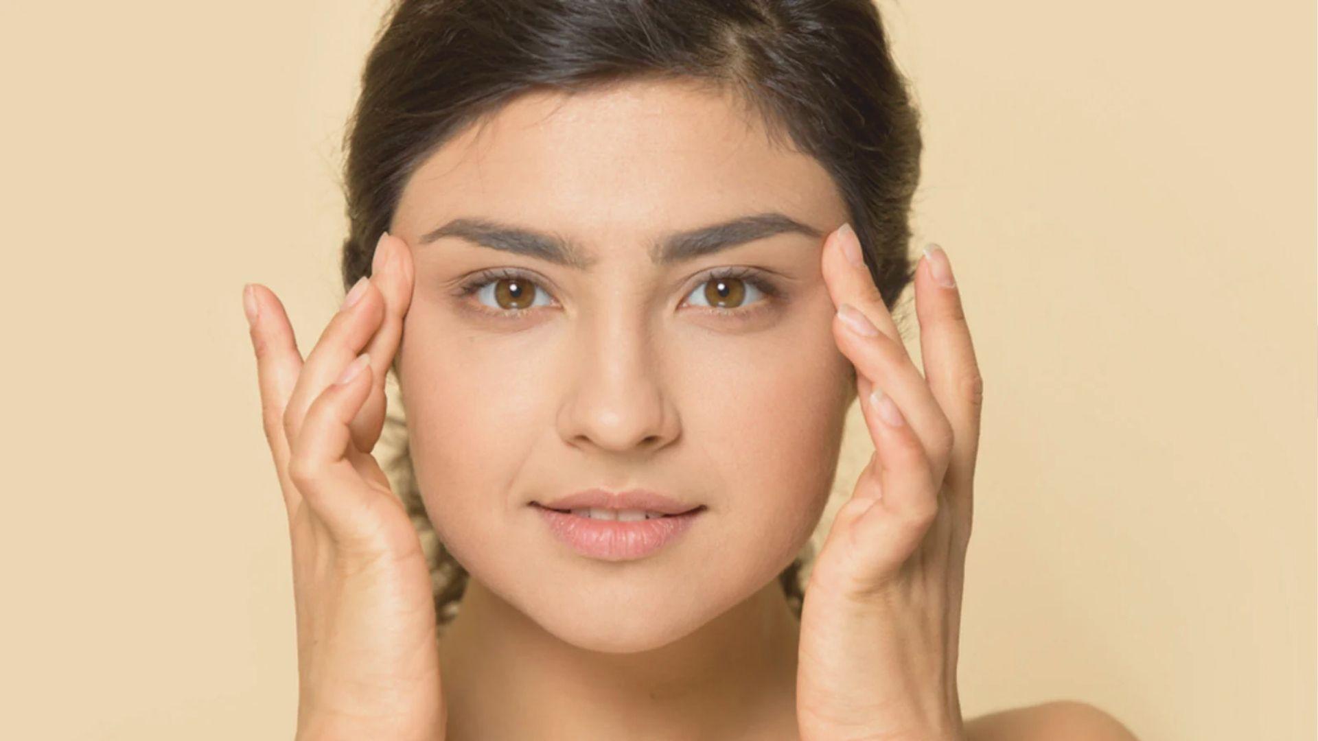 Close-up of a woman touching her clear, healthy skin against a beige background.