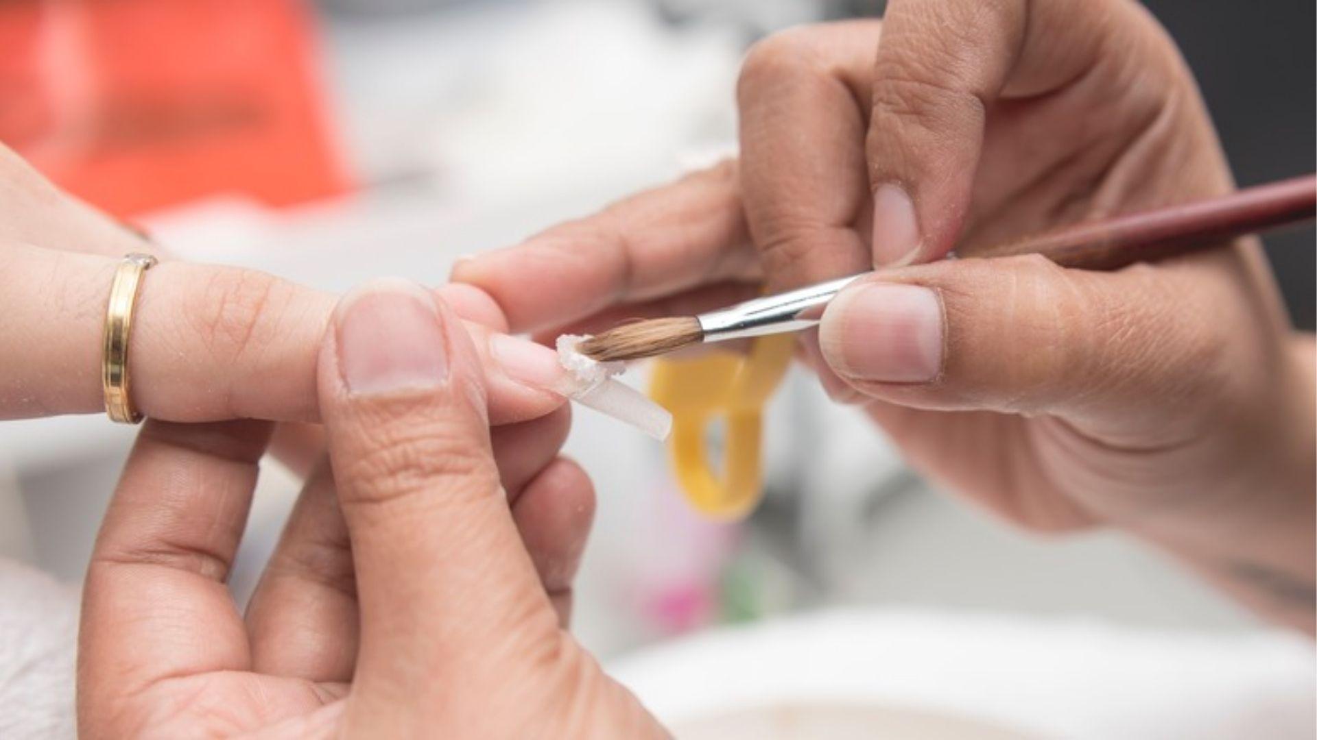 Applying solar acrylic mix to nail extension; solar nails are tough, lasting false nail enhancements.