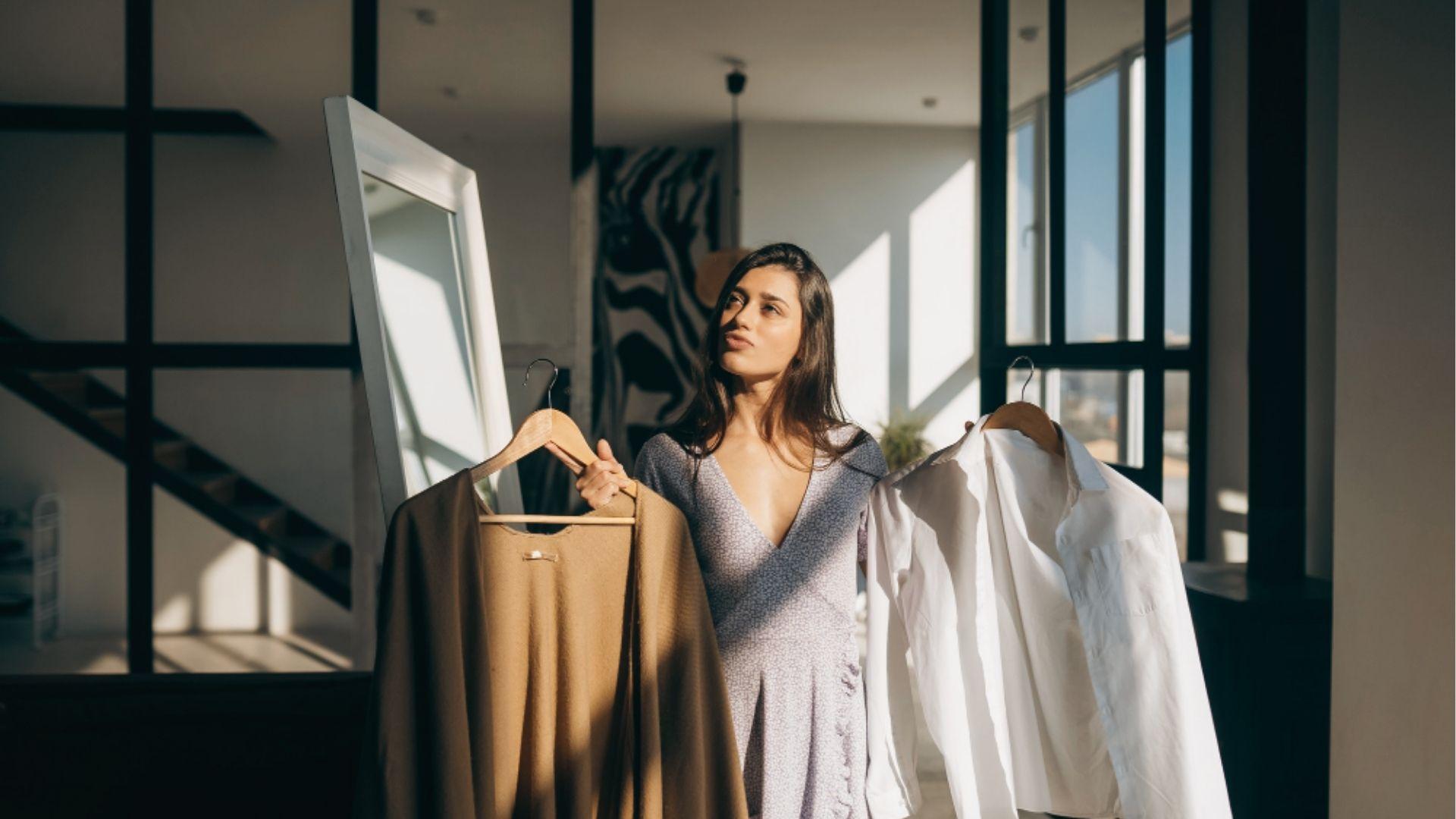 Woman holding hangers with tan cardigan and white button-down, choosing loose layers for post tan