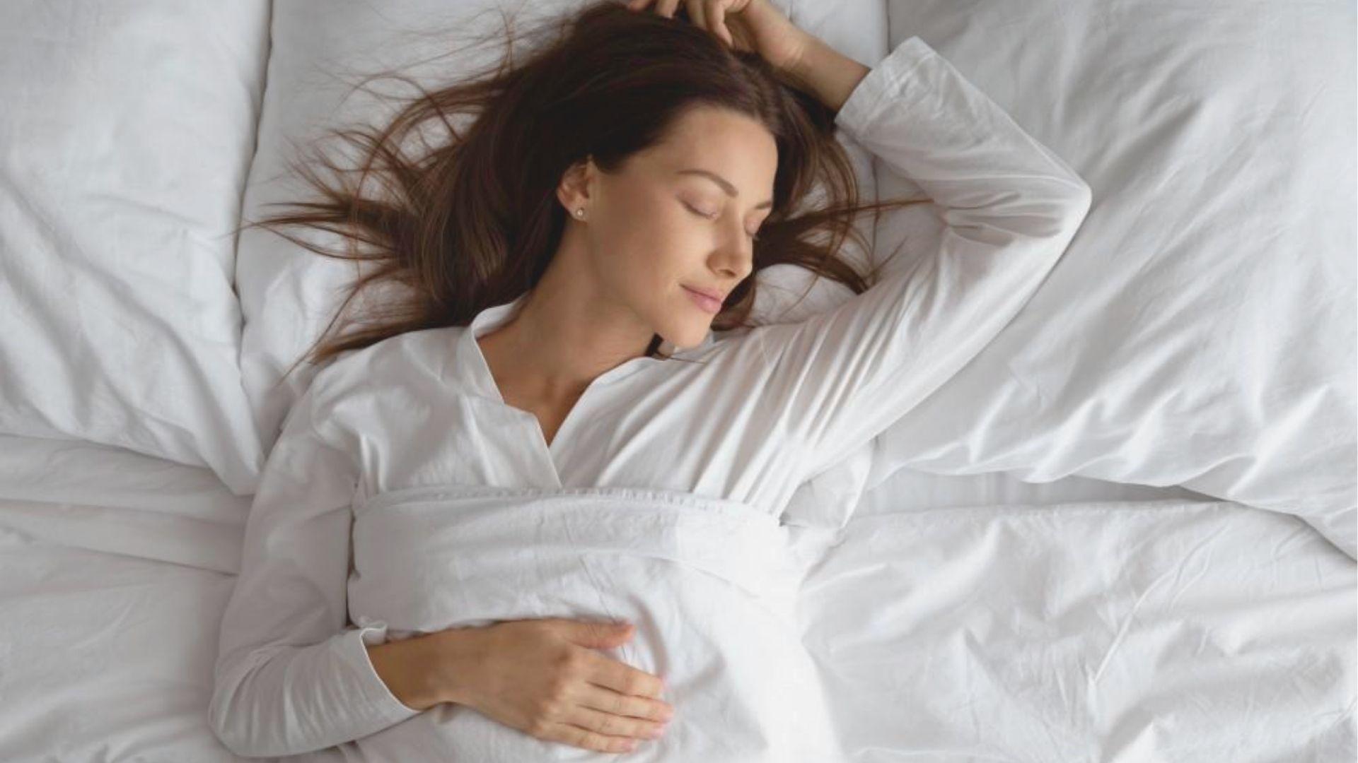 Overhead view of a peaceful woman sleeping on white bedsheets in a white nightgown.