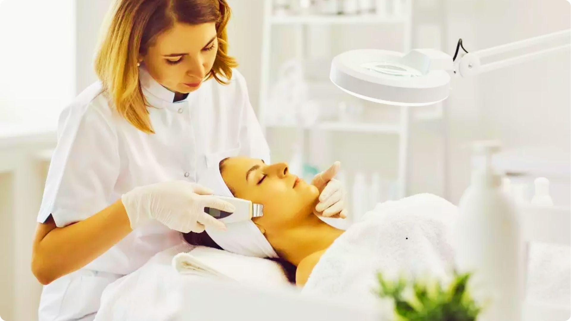 Skincare professional using a handheld device on a client's face under a magnifying lamp.