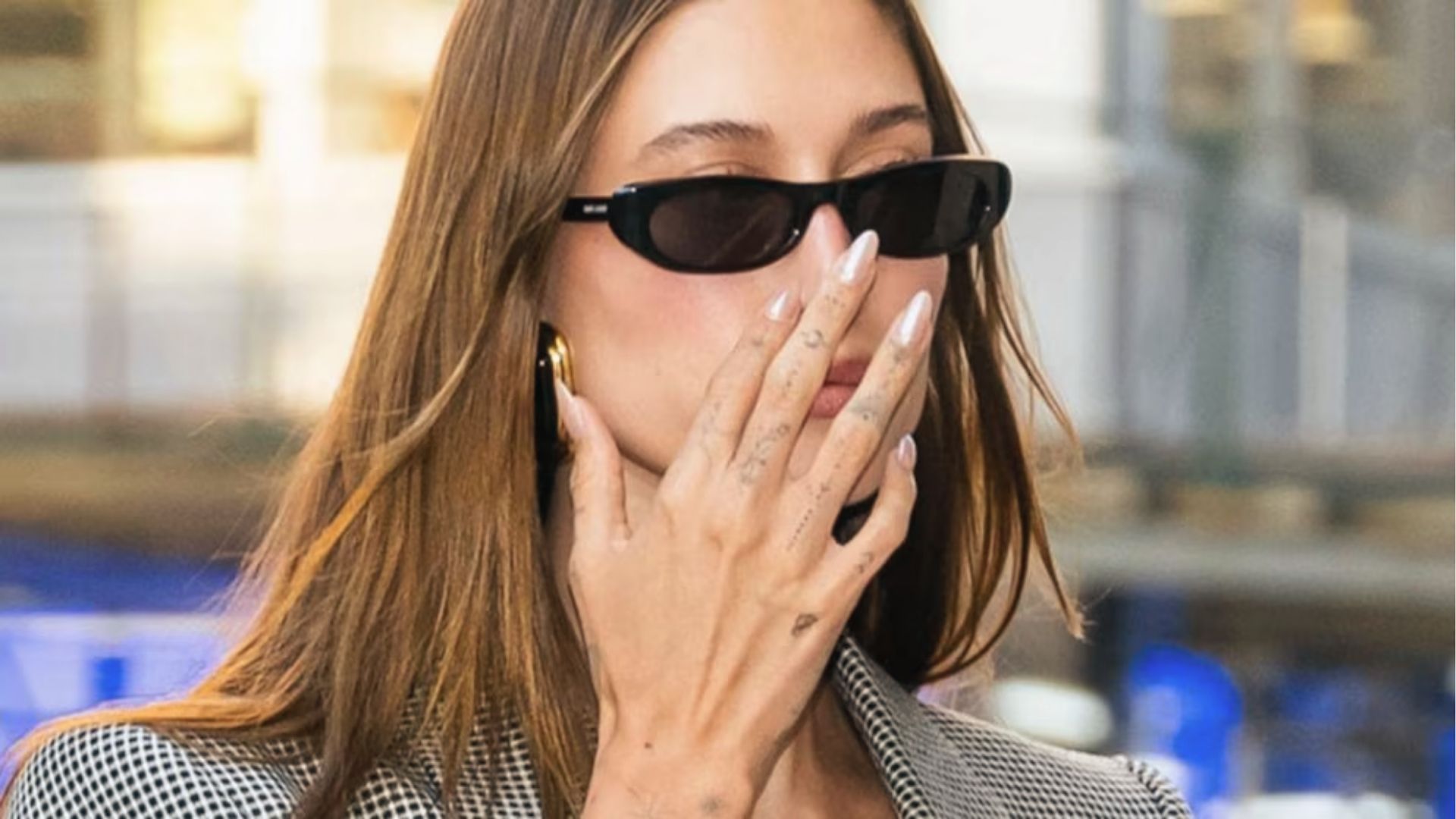 Hailey Bieber covers mouth with hand showing classic white chrome glazed donut nails