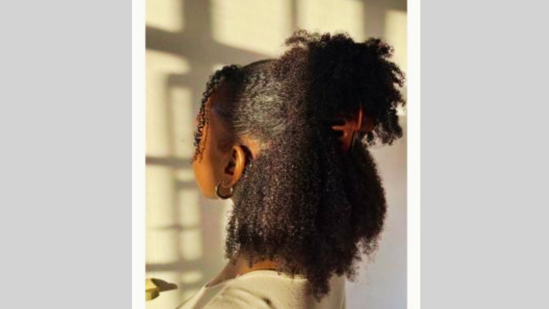 Woman with natural curls half up using large claw clip stands in sunlit room shadows
