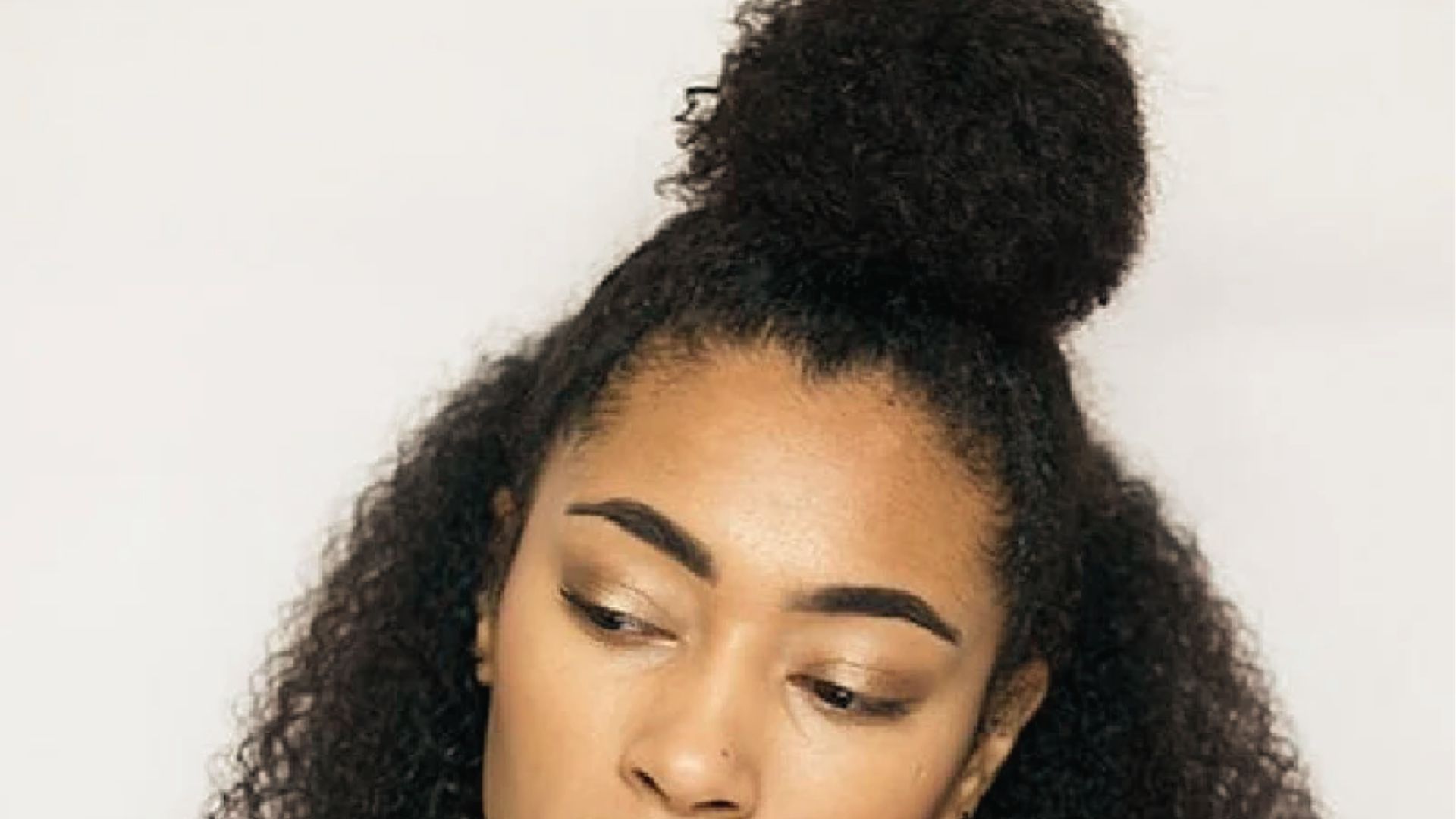 Half up half down style on curly black hair with high puff and soft edges on plain backdrop