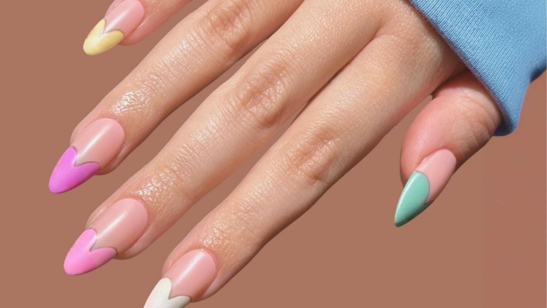 Almond-shaped gel nails with a nude-pink base and colorful heart French tips in pastel yellow, pink, mint, and white.