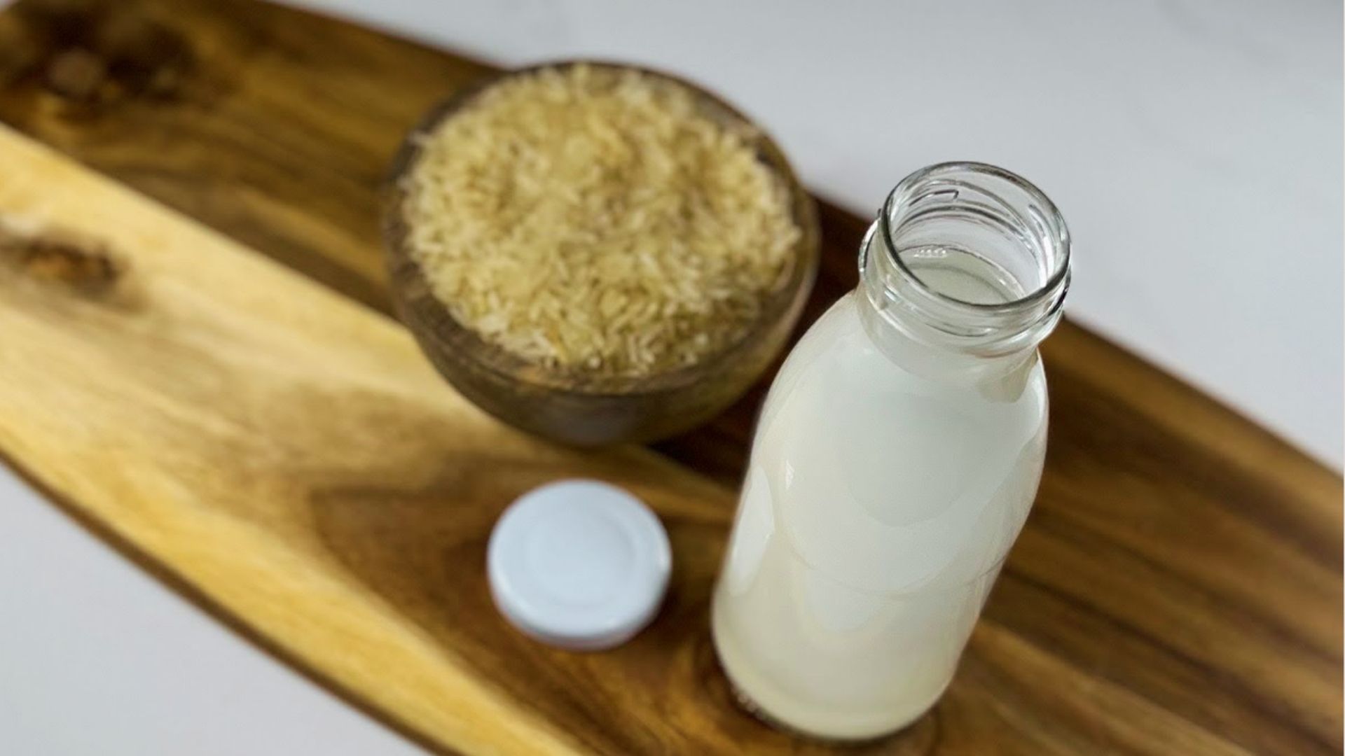 A bottle filled with rice water placed beside a bowl of raw rice used for hair care preparation