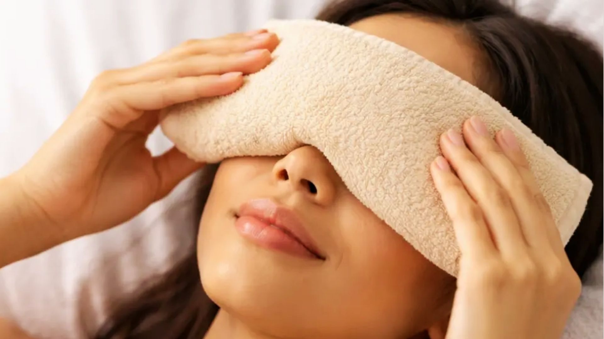 Person applying a warm compress to reduce swelling from a small bump under the eye.