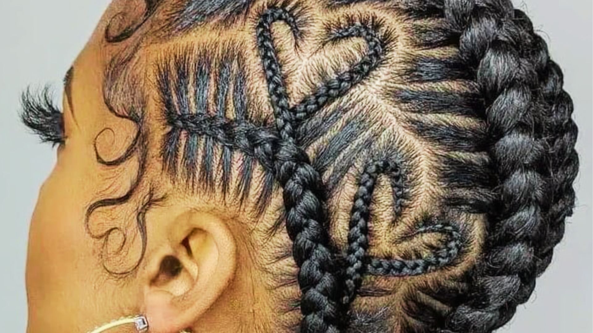 Close side view of intricate cornrow braids forming heart patterns with swirl edges styled up