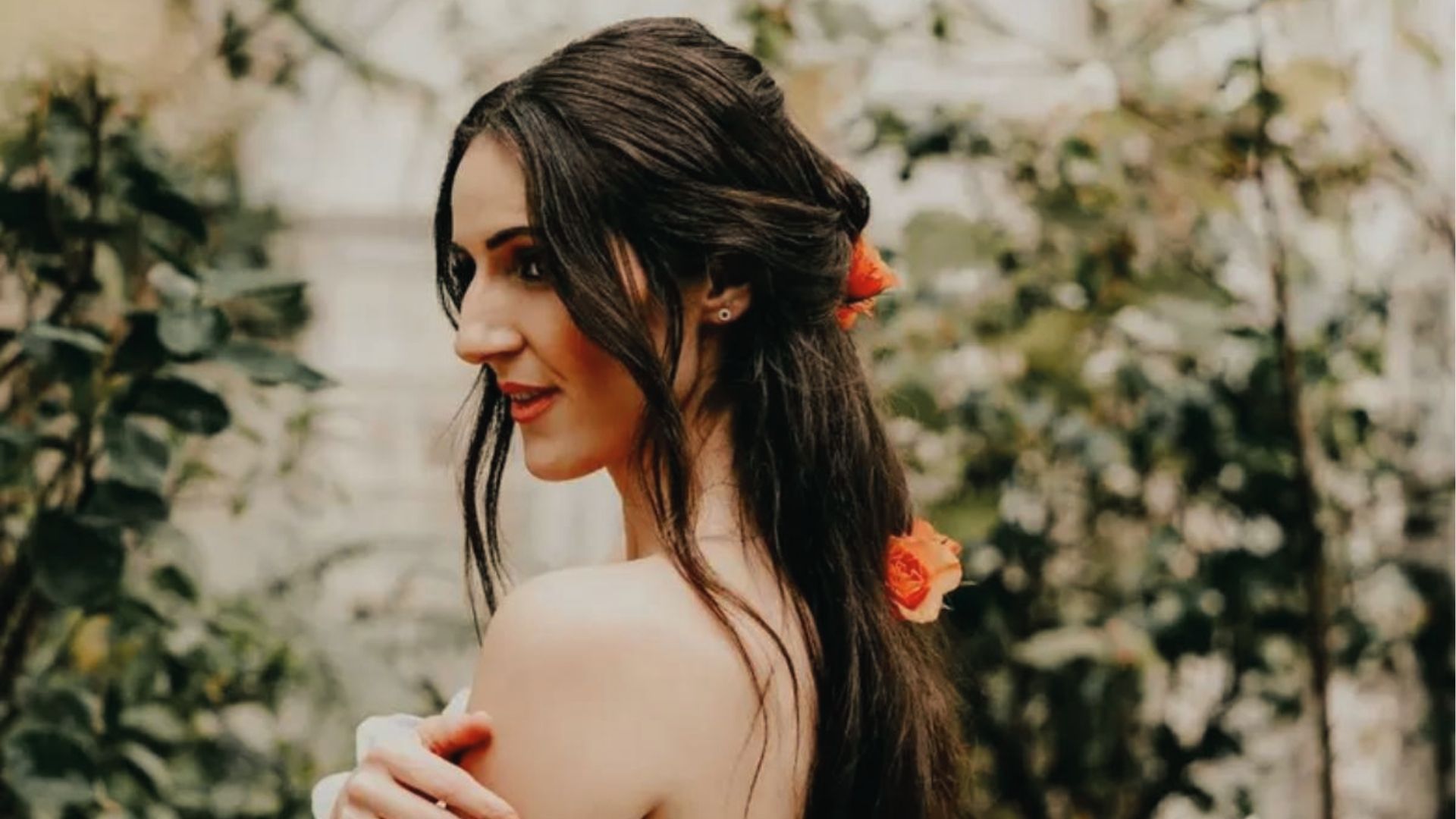 Garden half up half down black hairstyle with twisted sides, loose waves, and orange rose accents