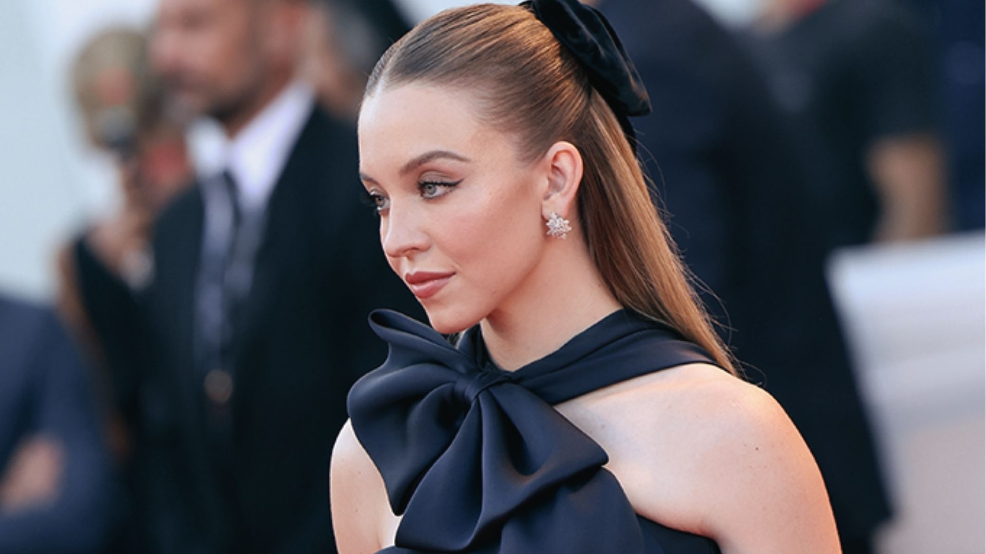 Glam half up half down black hairstyle with slicked crown, velvet bow, and straight hair at event