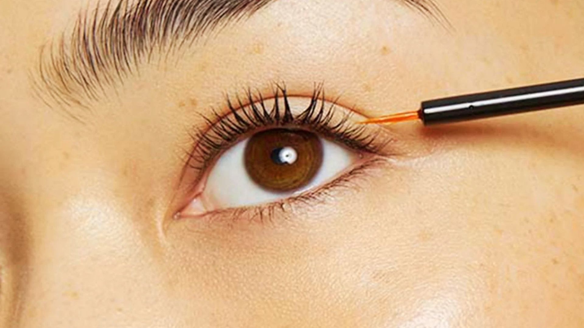 Close-up of a woman applying serum to her upper lash line using a precision applicator brush