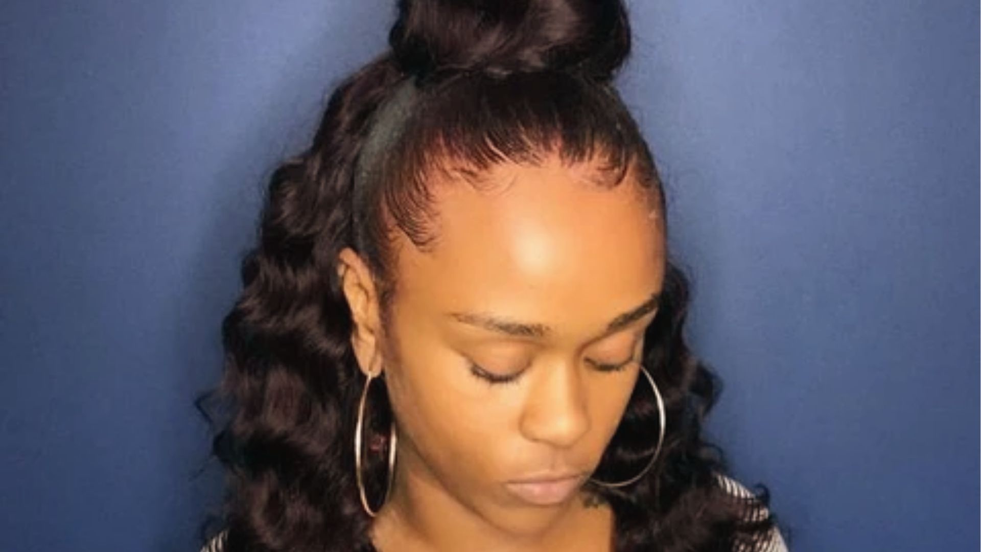 Sleek half up half down black hairstyle with high bun, loose waves, laid edges and gold hoops