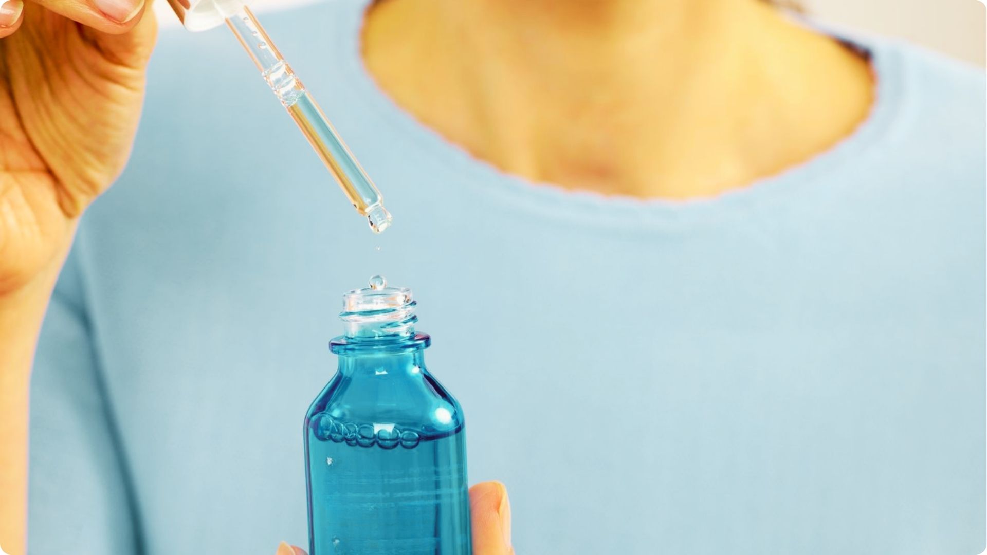 A person in a blue shirt holds a Hyaluronic Acid serum bottle as a dropper releases liquid above it.