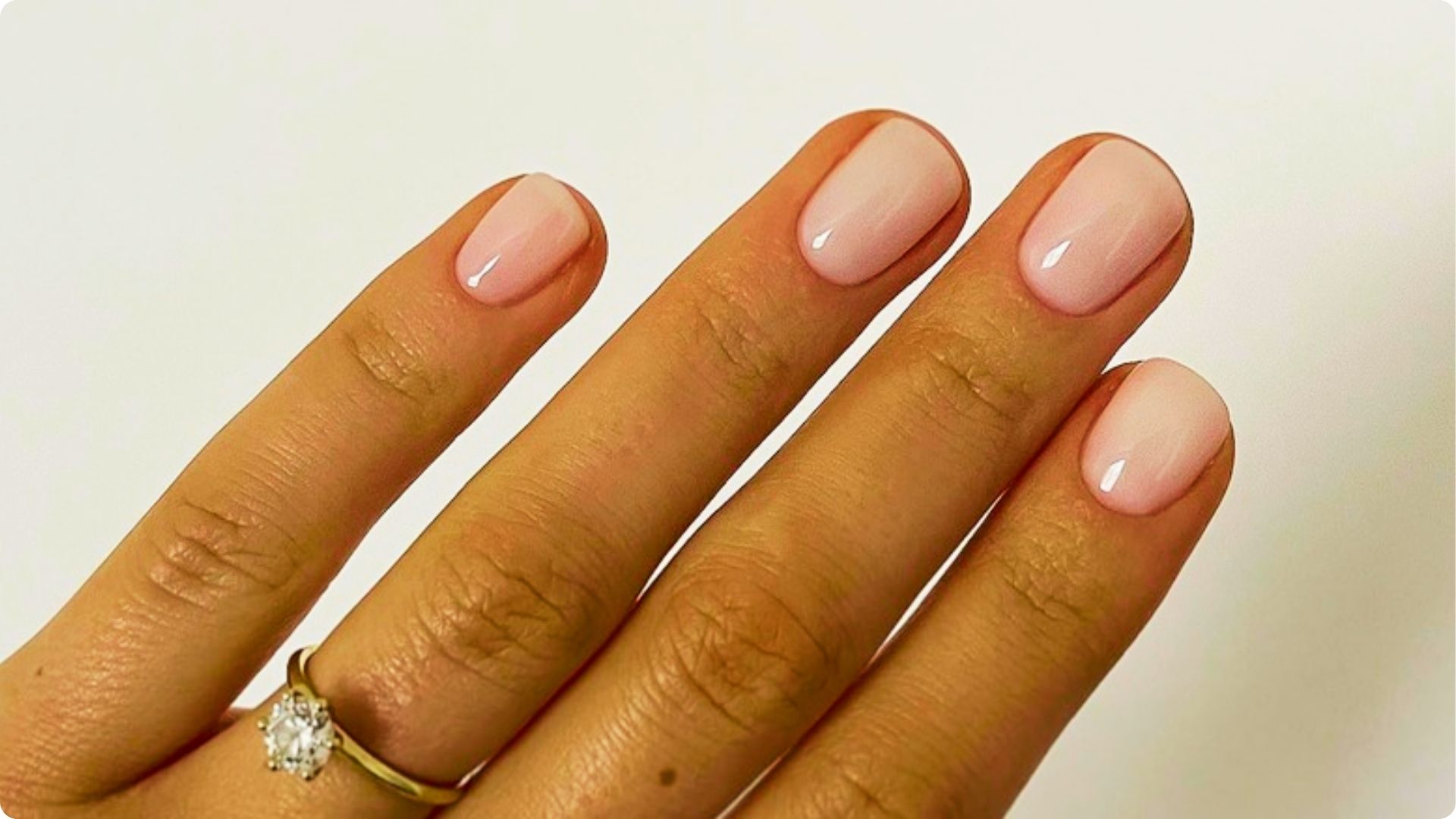 Close-up of a hand with short, round nails in sheer pink polish