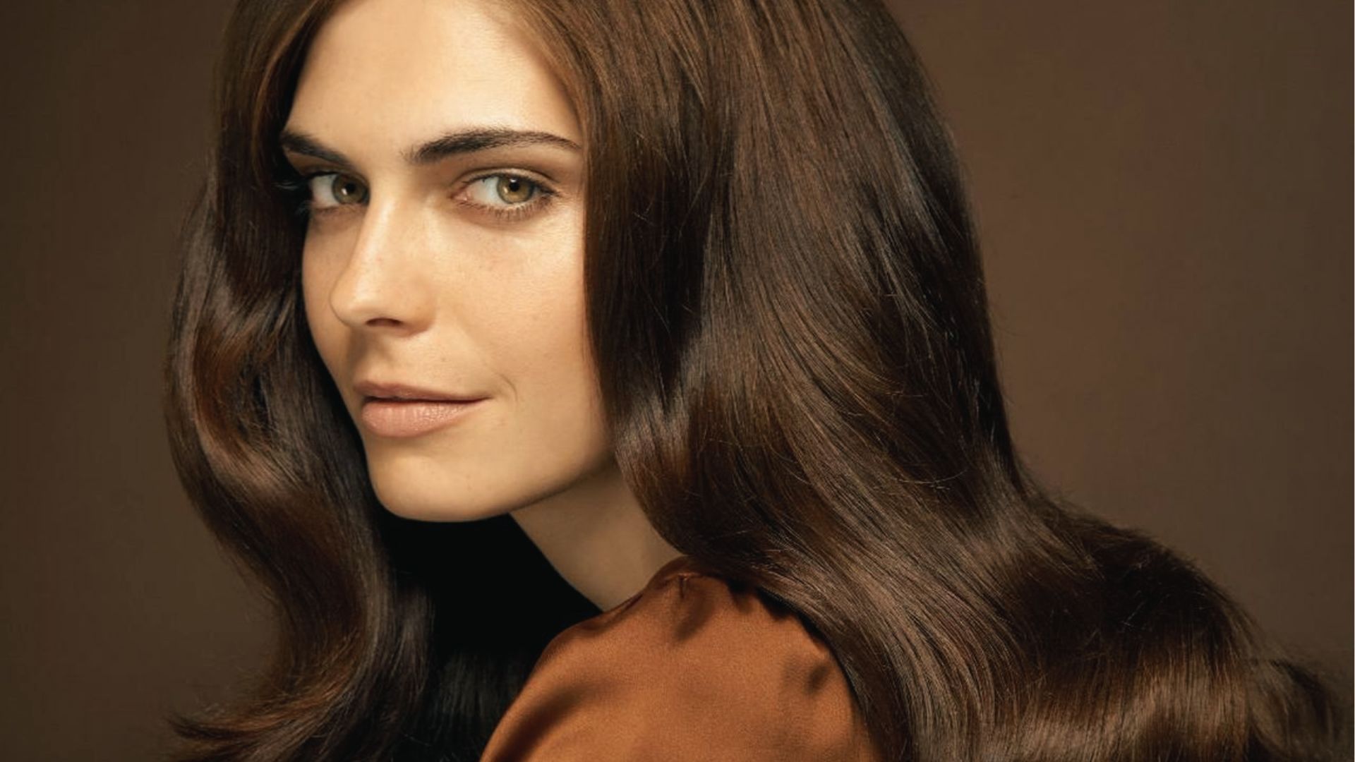 A woman with long glossy dark brown hair looking over shoulder
