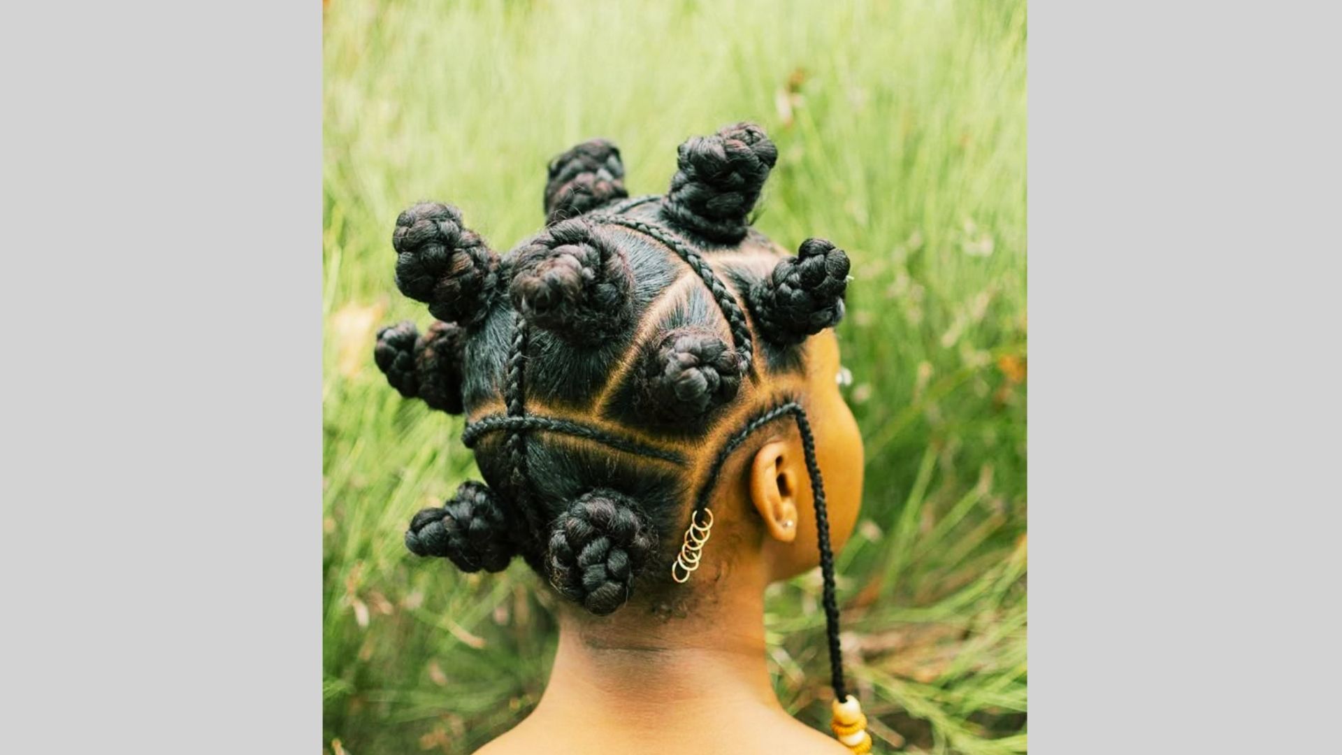 Rear view of child with Bantu knot braids and beaded strand in green grass field