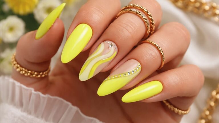 Long stiletto nails in neon yellow with white swirls and crystal accents, gold rings and flowers
