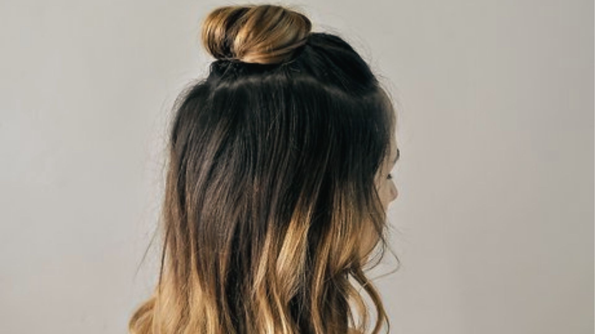 Sleek half up half down black style with high top bun and long ombre waves on plain backdrop
