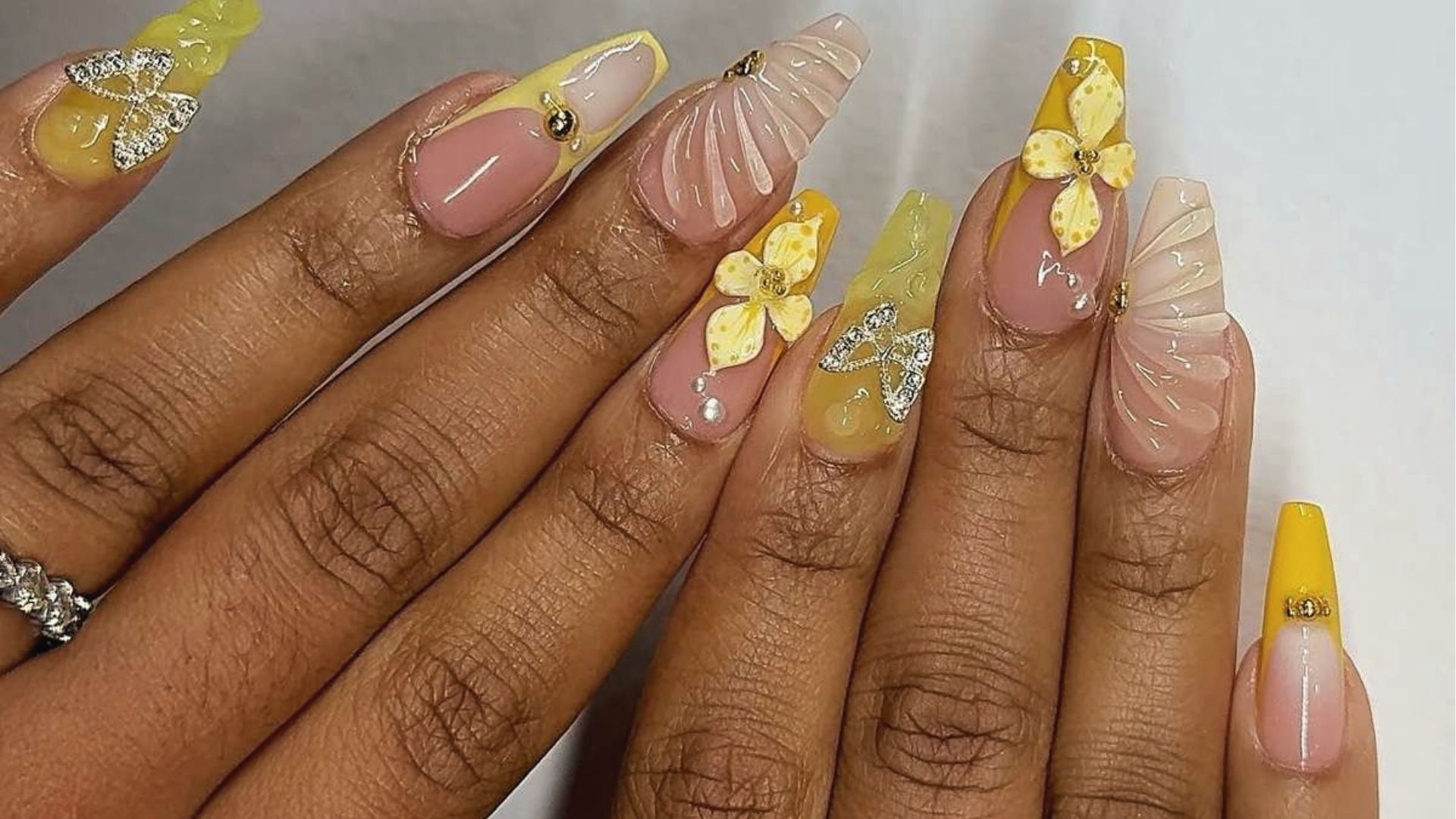 Long coffin nails with 3D yellow flowers, shell texture, rhinestones and gold gems on nude base