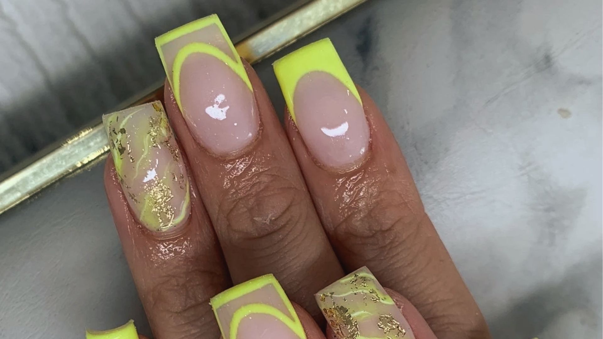 Square nails with neon yellow French tips, marble swirls and gold foil accents on a clear base.