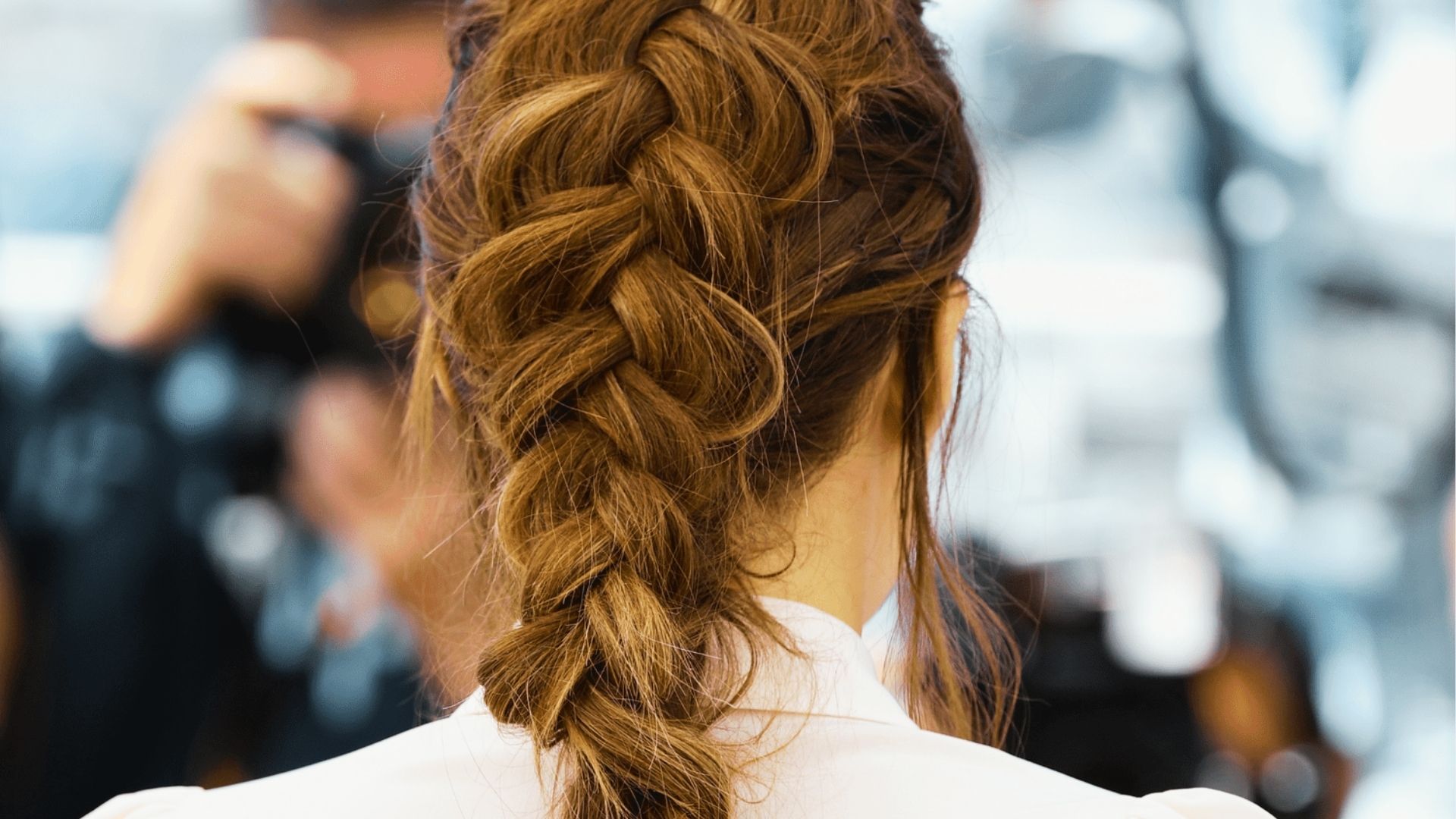 Rear view of woman with thick textured French braid updo at event with blurred cameras behind