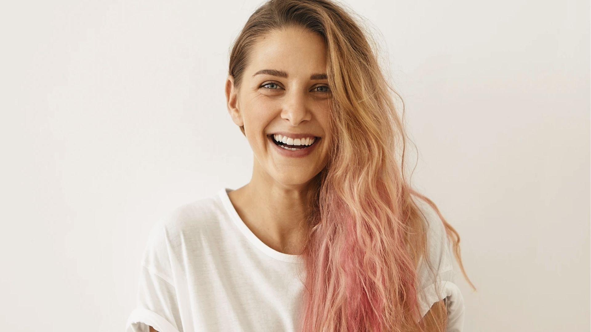 A smiling woman with pink-tinted light brown hair in white tee