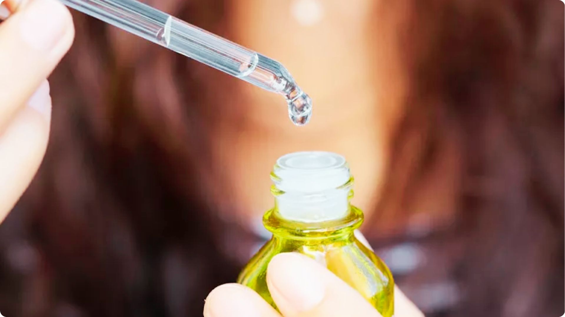 Close-up of a dropper releasing Vitamin C serum into a small amber glass bottle held by fingers.