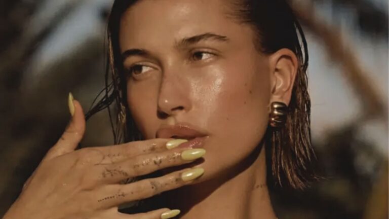 Hailey Bieber poses with wet hair showing butter yellow glazed donut nails and gold earring