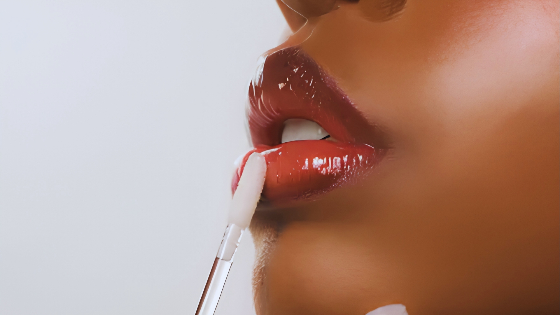 Side profile of glossy red lips with white applicator applying lip plumper gloss for hydration and volume.