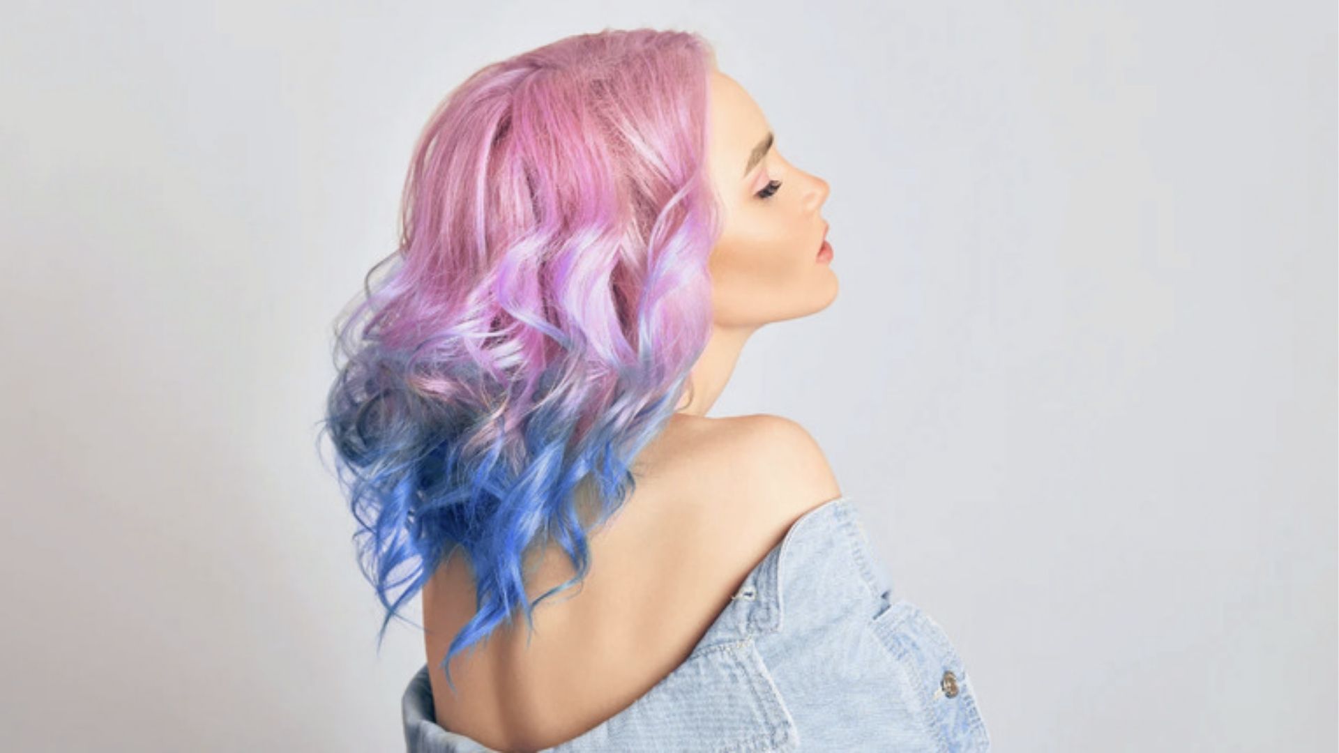 Curly pink to blue ombre hair in a denim jacket. Bright semi permanent shades.