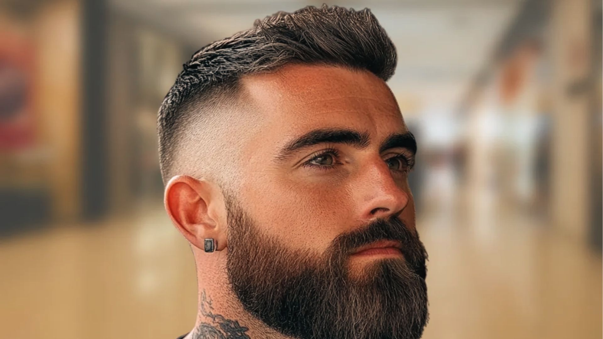 A man with a full beard sports a high fade that cuts tight above ears for bold, modern contrast.