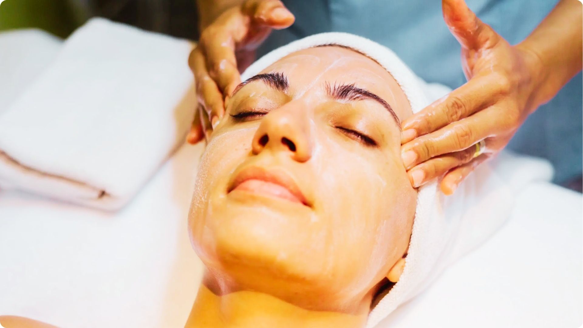 Close-up of a woman relaxing during a facial massage at a spa with eyes closed and towel on head