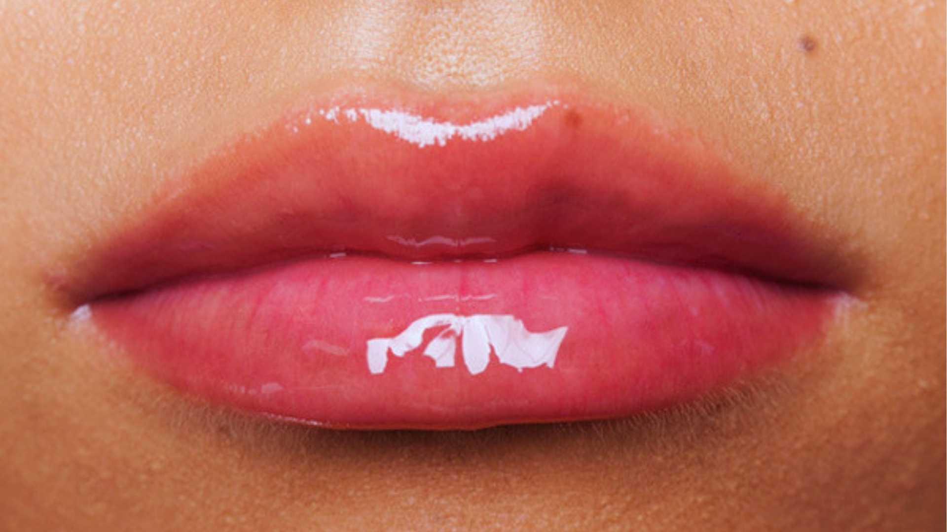 Extreme close-up of full glossy pink lips showing lip plumper results with shine and increased volume effect.