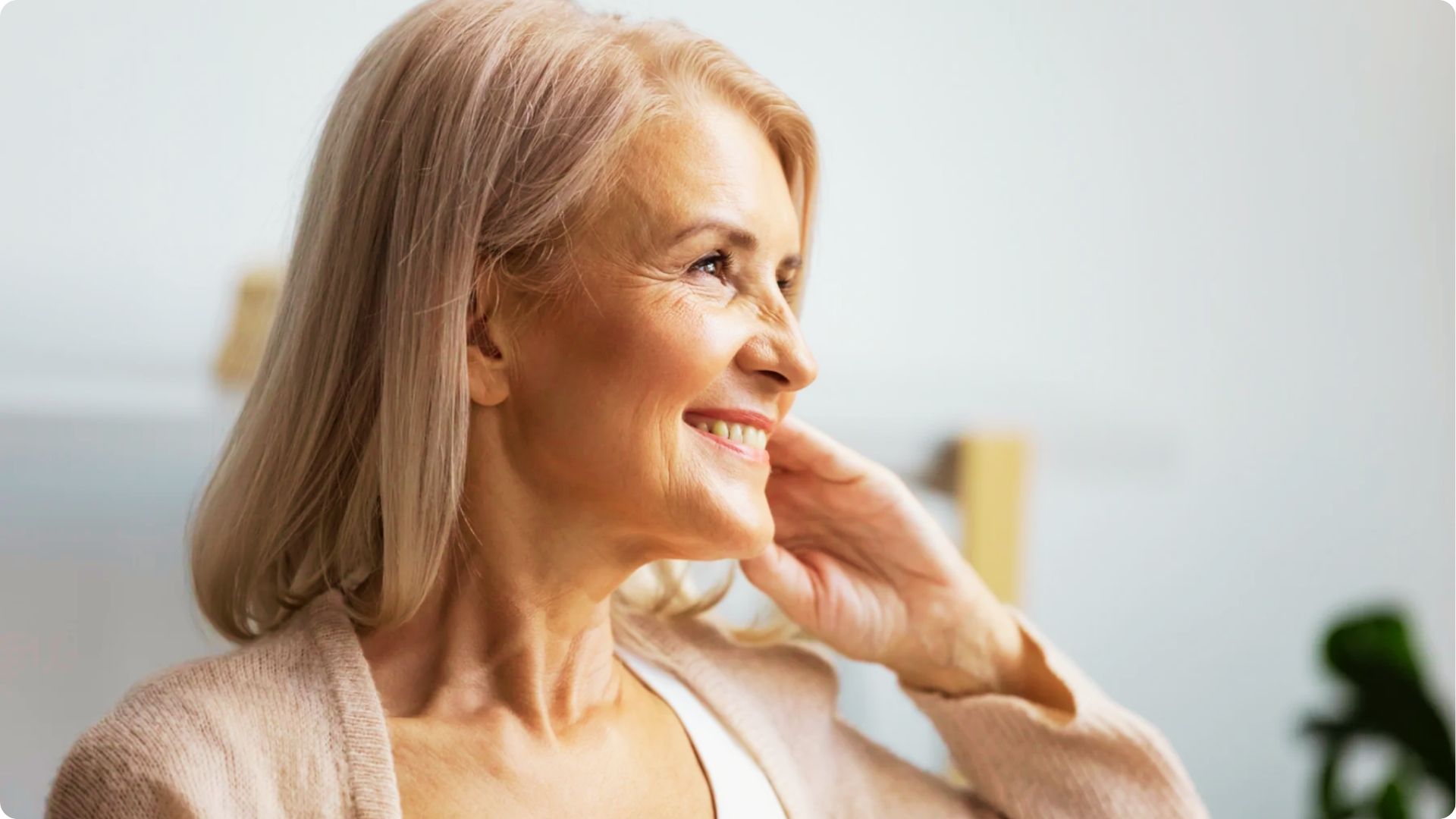 Profile view of a smiling mature woman with blonde hair touching her cheek, showing neck crepiness.