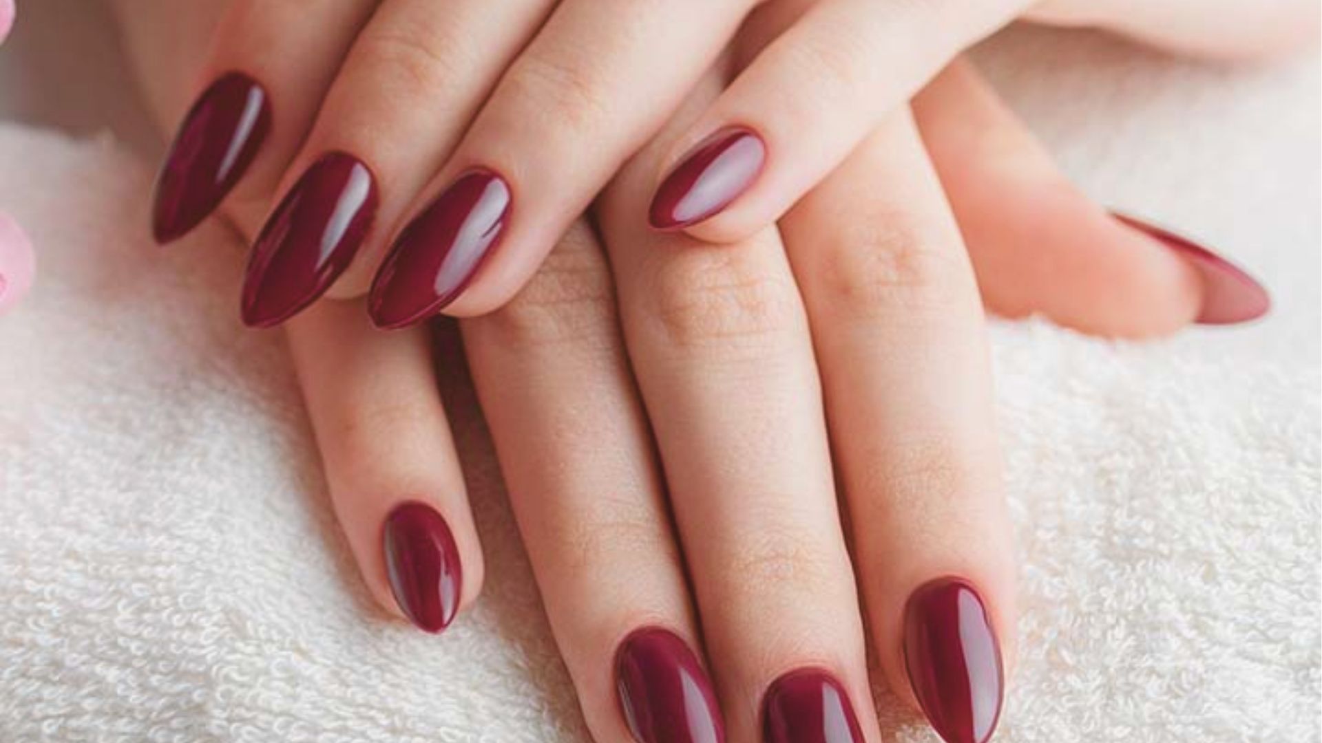 Long almond-shaped gel nails coated in deep burgundy polish with a glass-like shine.