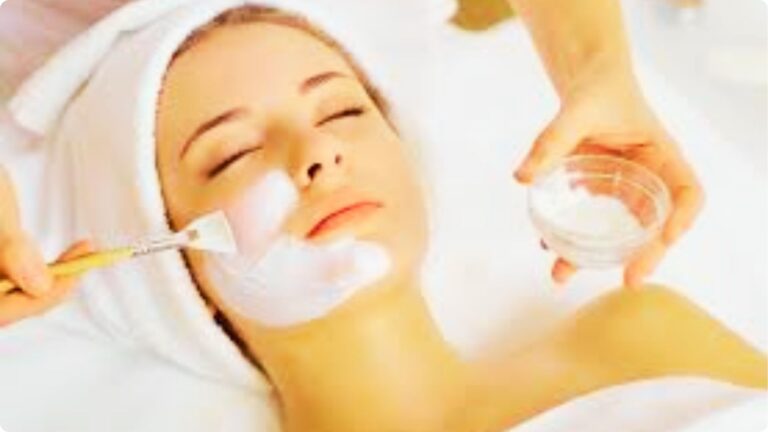 Relaxed client with eyes closed receiving a facial mask application from an esthetician with a brush.
