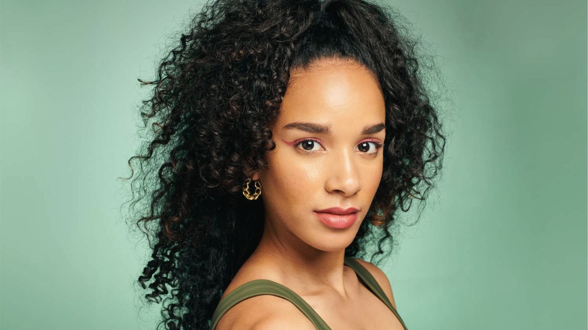 Woman with Short Curly Half Up Hairstyle in green tank top with golden hoop earrings