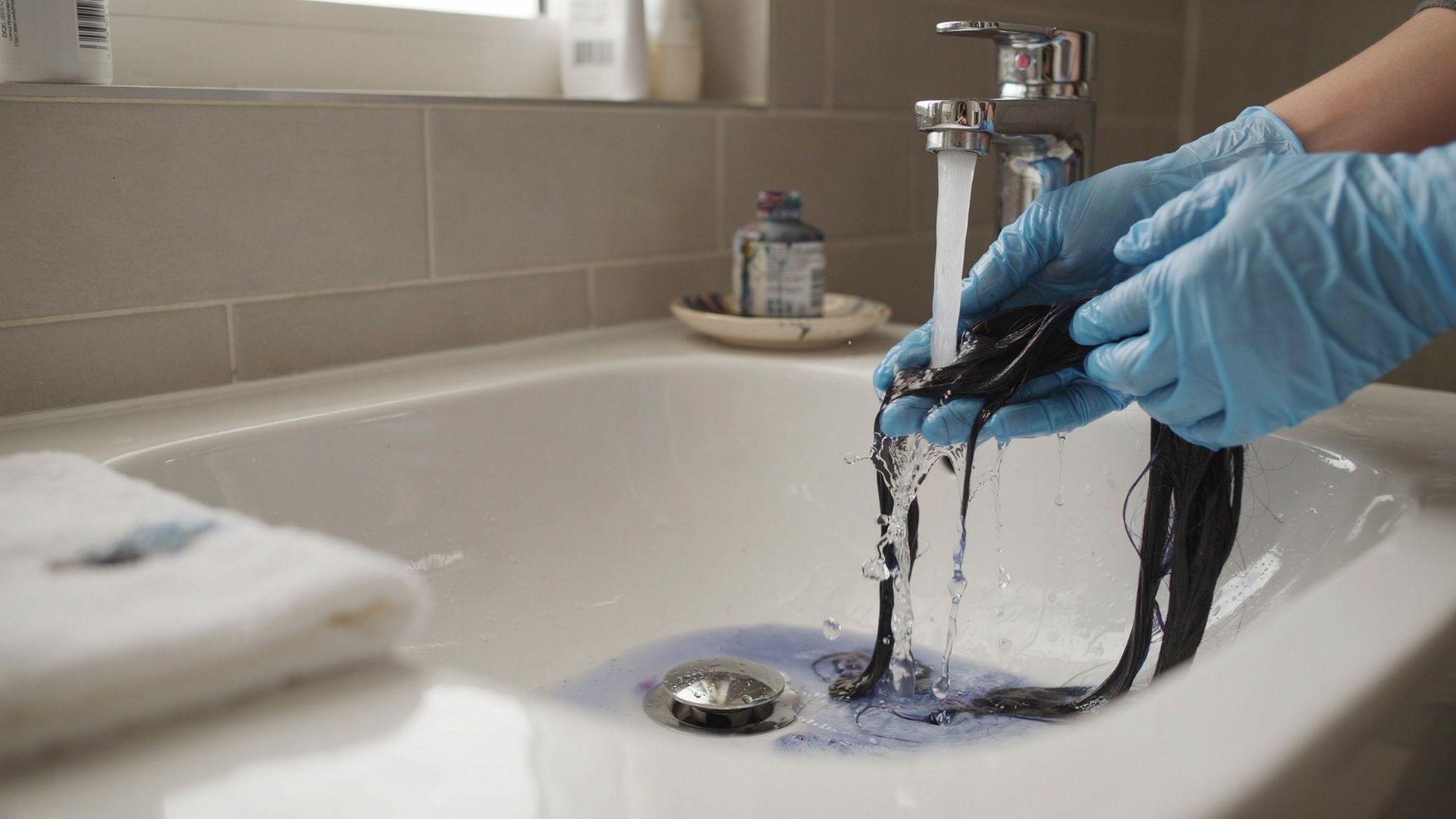 Rinsing synthetic hair under cool water to remove excess dye.