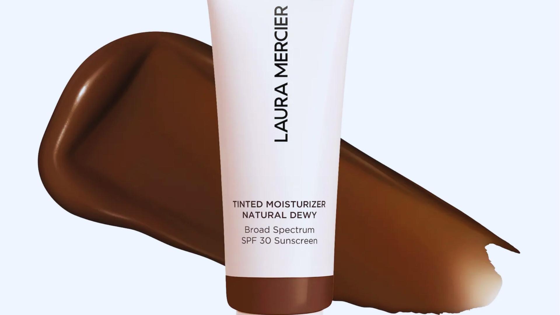 Laura Mercier Tinted Moisturizer Natural Dewy SPF 30 tube stands before rich brown product smear showing deep shade and creamy texture.
