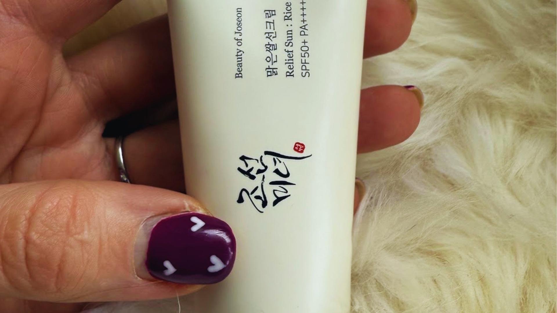 Close-up of hand with purple heart nail art holding Beauty of Joseon Relief Sun Rice + Probiotics SPF50+ tube over faux fur.