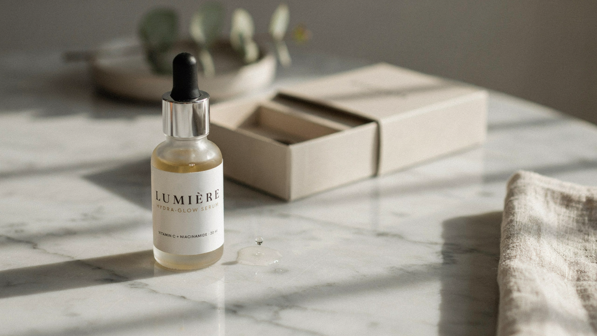 Lumière Hydra-Glow Serum with Vitamin C and Niacinamide in a dropper bottle on a sunlit marble surface with gift box.