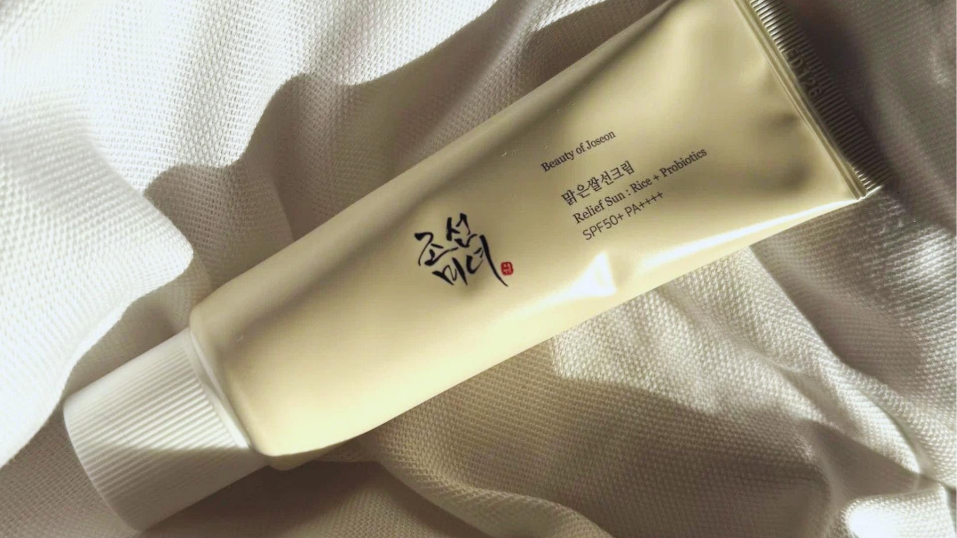 Beige tube of Beauty of Joseon Relief Sun Rice + Probiotics SPF50+ PA++++ rests on textured white fabric in natural sunlight.