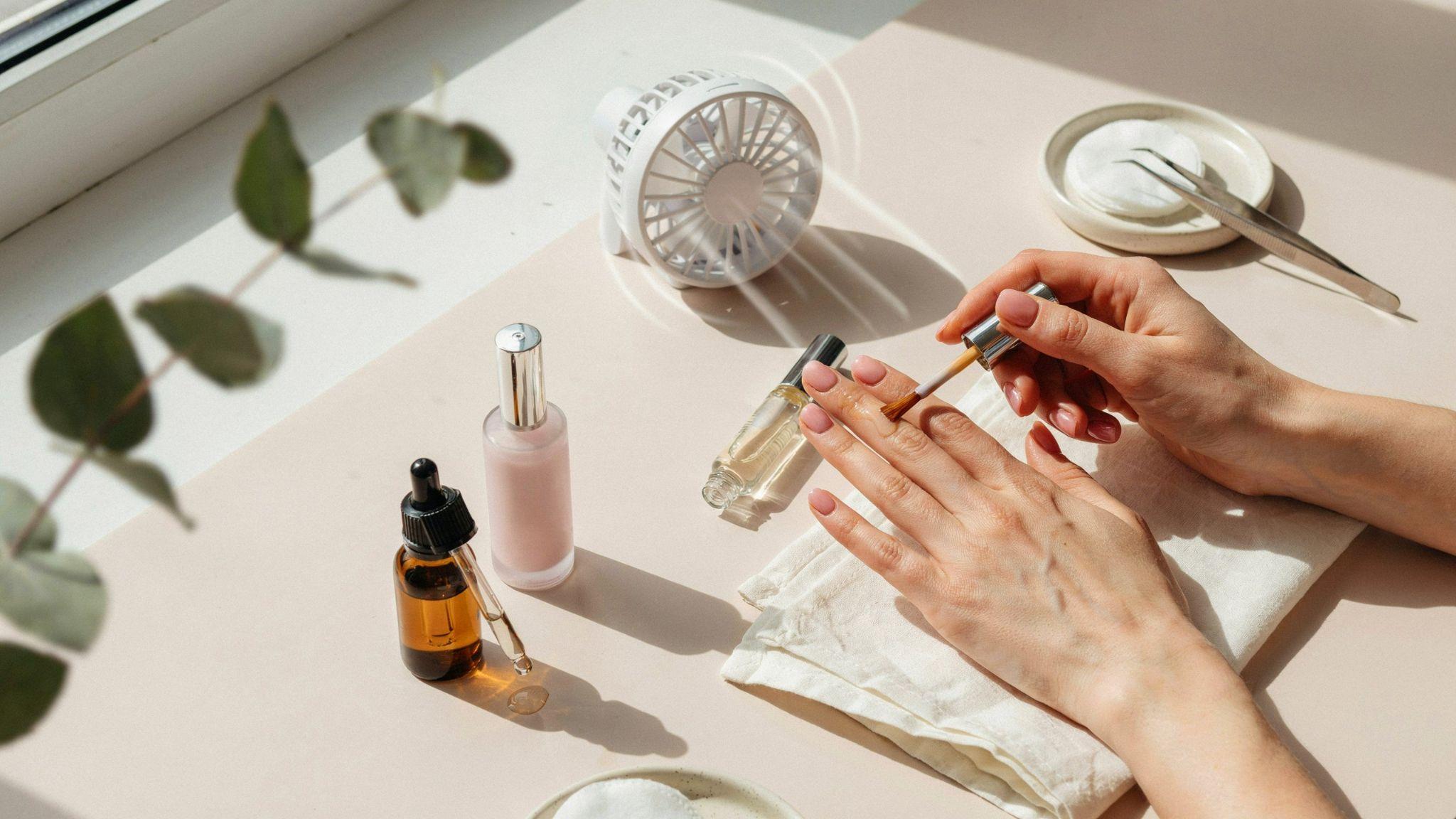 Freshly painted nails drying with fan, top coat, and manicure drying products