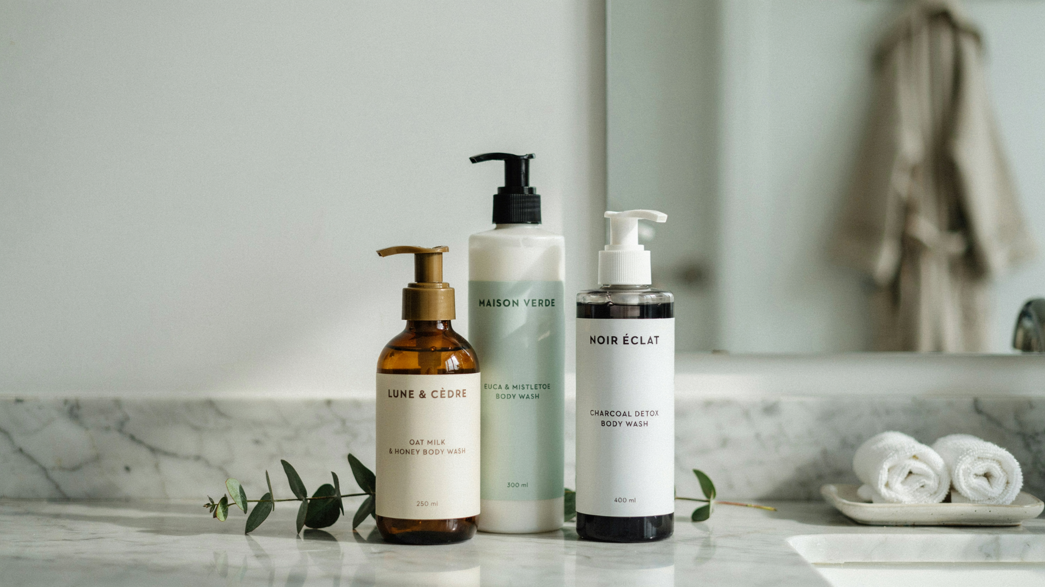 Three premium body wash bottles displayed on a marble bathroom counter.